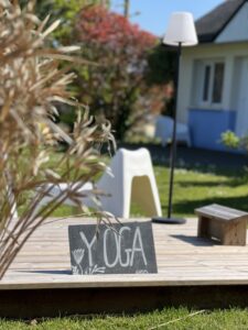 Planche de yoga sur terrasse en bois dans le jardin de l’Hôtel Heod avec chaise et lampe extérieure